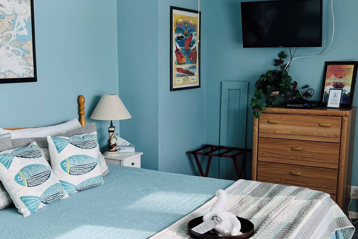 A bedroom with a bed, a ceiling fan, a TV, a dresser, and a map on the wall.