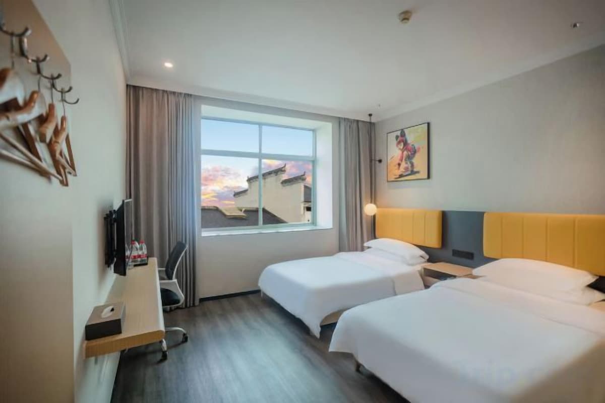 A hotel room with two beds, a desk with a chair, a television, and a window with curtains.