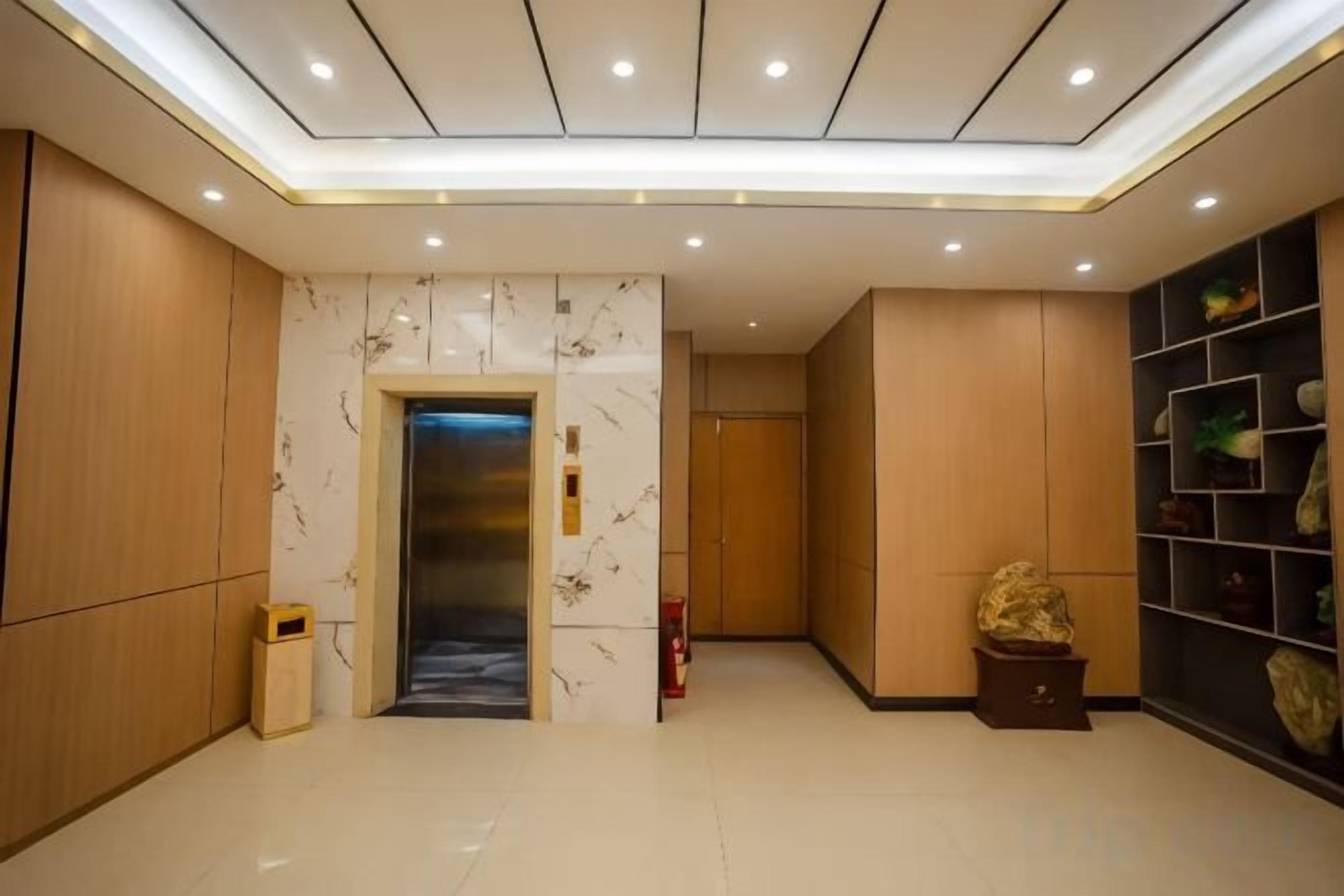 Rebedor d'hotel amb una paret de marbre, un ascensor, un safataire i una estant amb objectes decoratius.