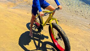 A person riding a bicycle on a sandy beach with clear water in the background. - Villa Flecheiras  (Trairi)