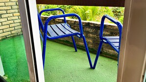 A view through a glass door of a balcony with two blue metal chairs and a stone wall. - Villa Flecheiras  (Trairi)
