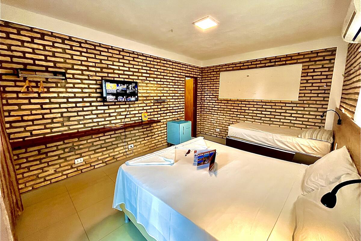 Une chambre d’hôtel avec un mur en briques, un téléviseur à écran plat, un lit, une table de chevet et une armoire.