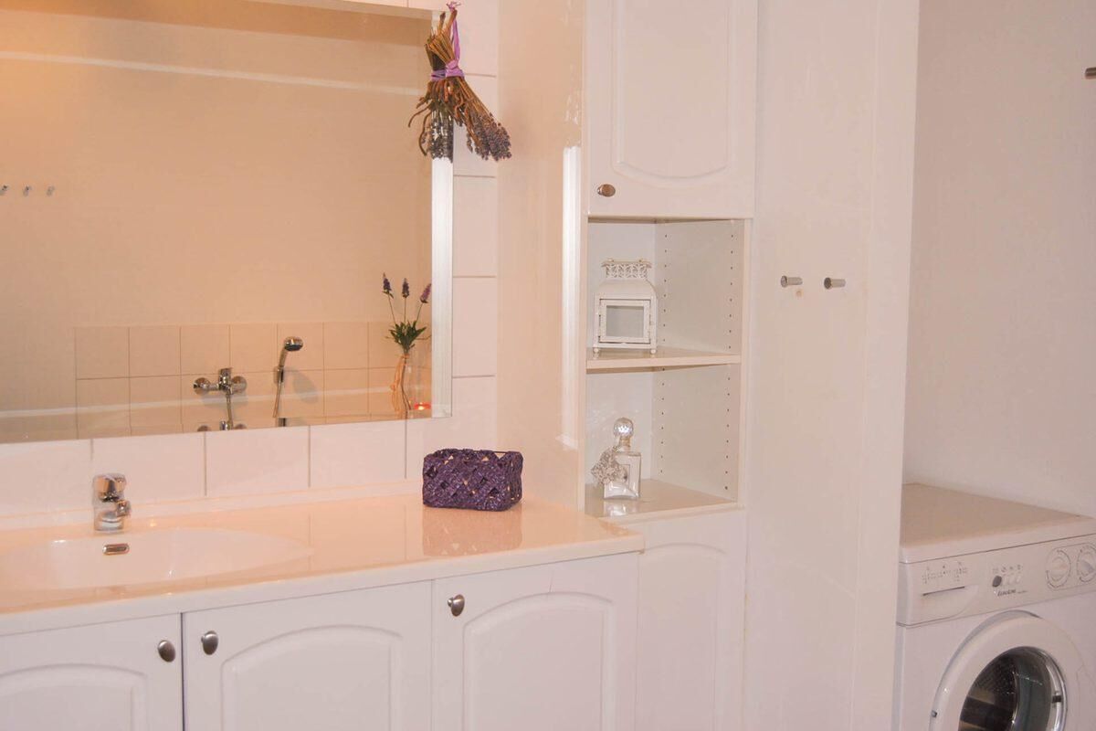 Un baño con lavamanos blanco, espejo y lavadora.