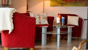 A red sofa with a white throw blanket, a glass coffee table, and a decorative candle. - FH „Kajüte“81m², 4 Pers. im Marinapark Scharmützelsee, Sauna, Whirlpool, Kamin (Wendisch Rietz Siedlung)