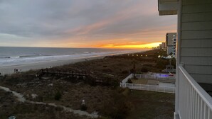 A beach view with a wooden boardwalk, a white fence, and a building with a balcony. - Ocean front at the chateau (North Myrtle beach)