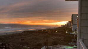 A sunset view from a balcony overlooking a beach with a boardwalk and buildings in the background. - Ocean front at the chateau (North Myrtle beach)