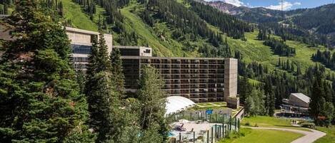 A hotel with a modern design, surrounded by lush green hills and mountains.