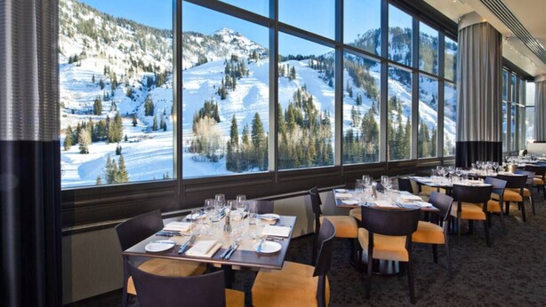 A restaurant with tables set for dining, large windows offering a view of a snowy mountain landscape.
