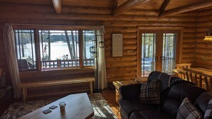 A cozy cabin interior with a wooden interior, a large window overlooking a snowy landscape, a couch, and a table with a jar of honey.