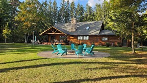 A log cabin with a porch, outdoor seating, and a stone chimney.