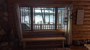 A cabin with a large window overlooking a lake, a wooden bench inside, and a sign with lake rules on the wall.