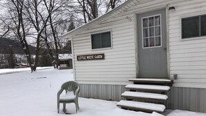 A cabin named "Little White Cabin" with a snow-covered porch and steps leading to the entrance. - Little White Cabin by the river, fishing trails, kayaking, near State Park lake  (Manns Choice)