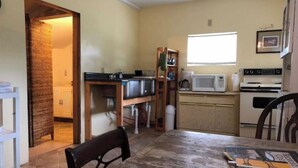 A compact kitchen with basic appliances, a dining table, and a small window. - Little White Cabin by the river, fishing trails, kayaking, near State Park lake  (Manns Choice)
