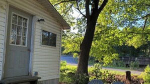 A small wooden cabin with a porch, two plastic chairs, and a tree in the background. - Little White Cabin by the river, fishing trails, kayaking, near State Park lake  (Manns Choice)