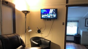 A living room with a leather sofa, a floor lamp, and a flat-screen TV mounted on the wall. - Horns Cabins - Allegheny Cabin by the roadside (Manns Choice)