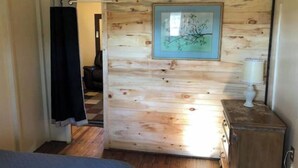 A room with a wooden wall, a framed picture, a lamp, and a bed. - Horns Cabins - Allegheny Cabin by the roadside (Manns Choice)