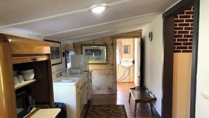 A compact kitchen with wooden cabinets, a countertop, and a dining area with a bench. - Horns Cabins - Allegheny Cabin by the roadside (Manns Choice)