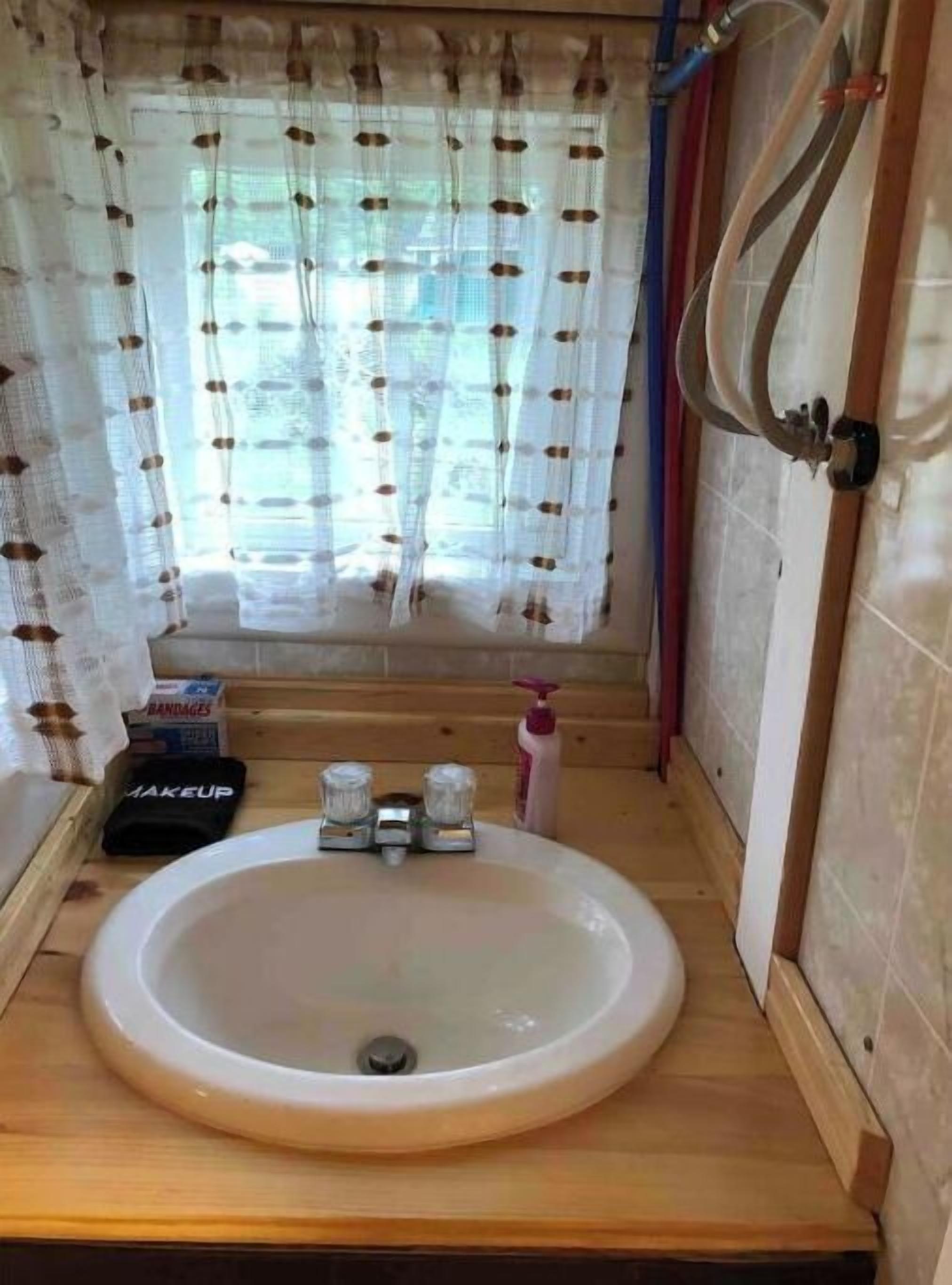A bathroom with a wooden vanity, a white sink, and a window with patterned curtains.
