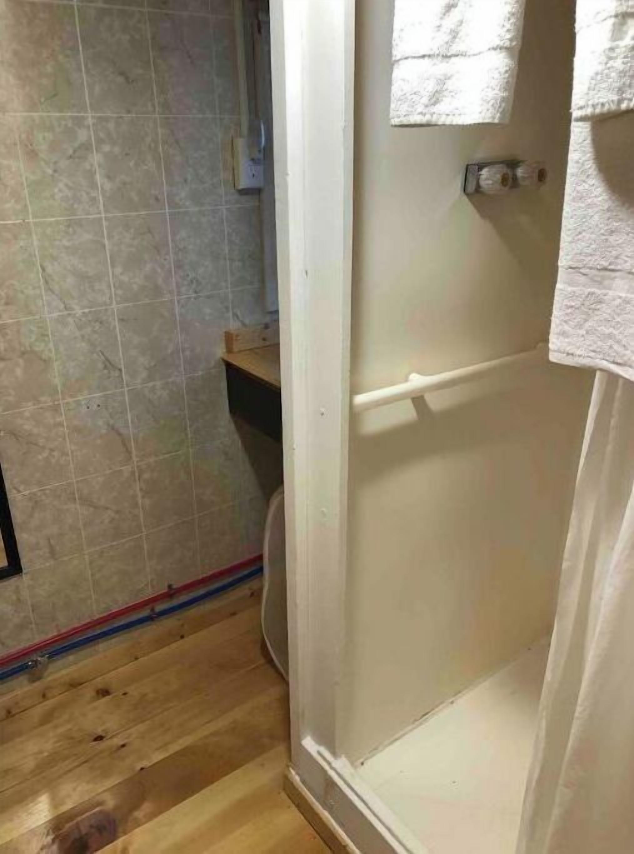 A bathroom with a shower, tiled walls, and wooden flooring.