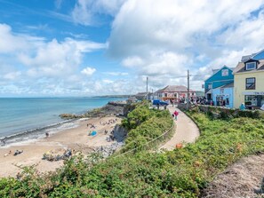 A coastal town with a sandy beach, a path leading to a pier, and buildings with visible signage.