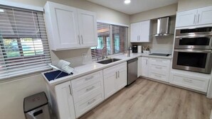 Una cocina moderna con armarios blancos, electrodomésticos de acero inoxidable y piso de madera.