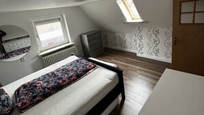 A bedroom with a bed, a dresser, a radiator, a window, and a door. - Small, cozy semi-detached house on a large plot (Heide)