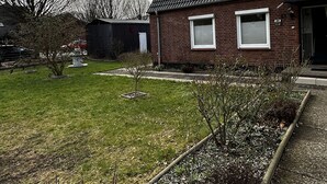 A residential house with a sloped roof, a small front porch, and a well-maintained lawn. - Small, cozy semi-detached house on a large plot (Heide)