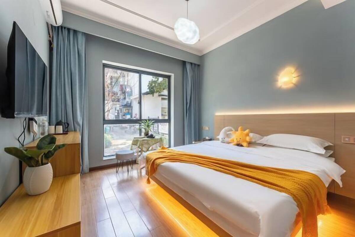 A modern hotel room with a large bed, a bedside table, a TV, and a window with curtains.
