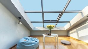 A high-ceiling room with a skylight, a blue bean bag, a small round table with a vase of flowers, and a round cushion. - wuginggu Hostel (Hangzhou)