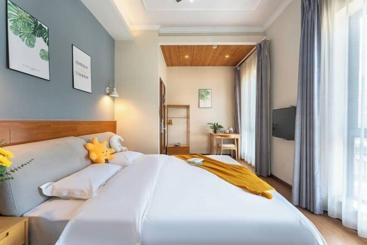 A hotel room with a bed, a desk, a chair, a TV, and a window with curtains.