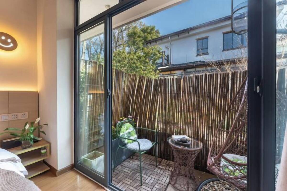 A modern room with a glass door leading to a balcony, a small table with a chair, and a bamboo fence.