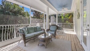 Eine überdachte Veranda mit einem Korbsessel, zwei Stühlen und einem Tisch.