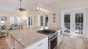Eine geräumige Küche mit einer zentralen Kochinsel, eine Essecke mit Tisch und Stühlen sowie ein Balkon mit Gartenmöbeln.