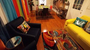 Una sala de estar con sofá, un sillón amarillo, una mesita de centro y un comedor con mesa y sillas.