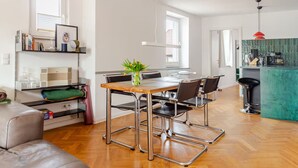 Een moderne keuken met een groen aanrecht, een eethoek met een houten tafel en metalen stoelen, en een zithoek met een bank en salontafel.