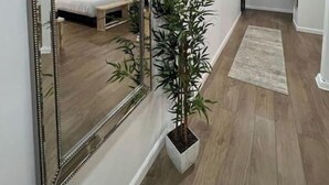 A modern hotel room with a large mirror, a bed with white bedding, a small bedside table, and a potted plant. - 🌟 Trendy & Private Basement Studio 🌟 (Puyallup)