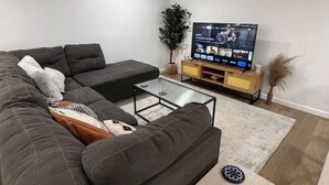 A modern living room with a sectional sofa, a coffee table, a flat-screen TV, and a wooden TV stand. - 🌟 Trendy & Private Basement Studio 🌟 (Puyallup)