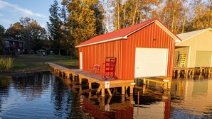 A red metal shed with a white garage door, situated on stilts over water, with a dock extending into the water. - Fish and Frolic – Lakefront w/Boathouse & Firepit (Scottsboro)