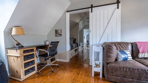 Une chambre à coucher confortable, aménagée en style « loft », avec un bureau en bois, un fauteuil de bureau noir, un canapé en cuir marron et une armoire blanche.