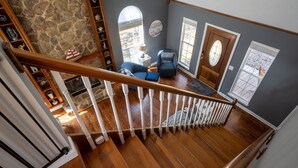 A wooden staircase with white balusters leading to a living area with a stone wall, a blue sofa, and a patterned rug. - Fish and Frolic – Lakefront w/Boathouse & Firepit (Scottsboro)