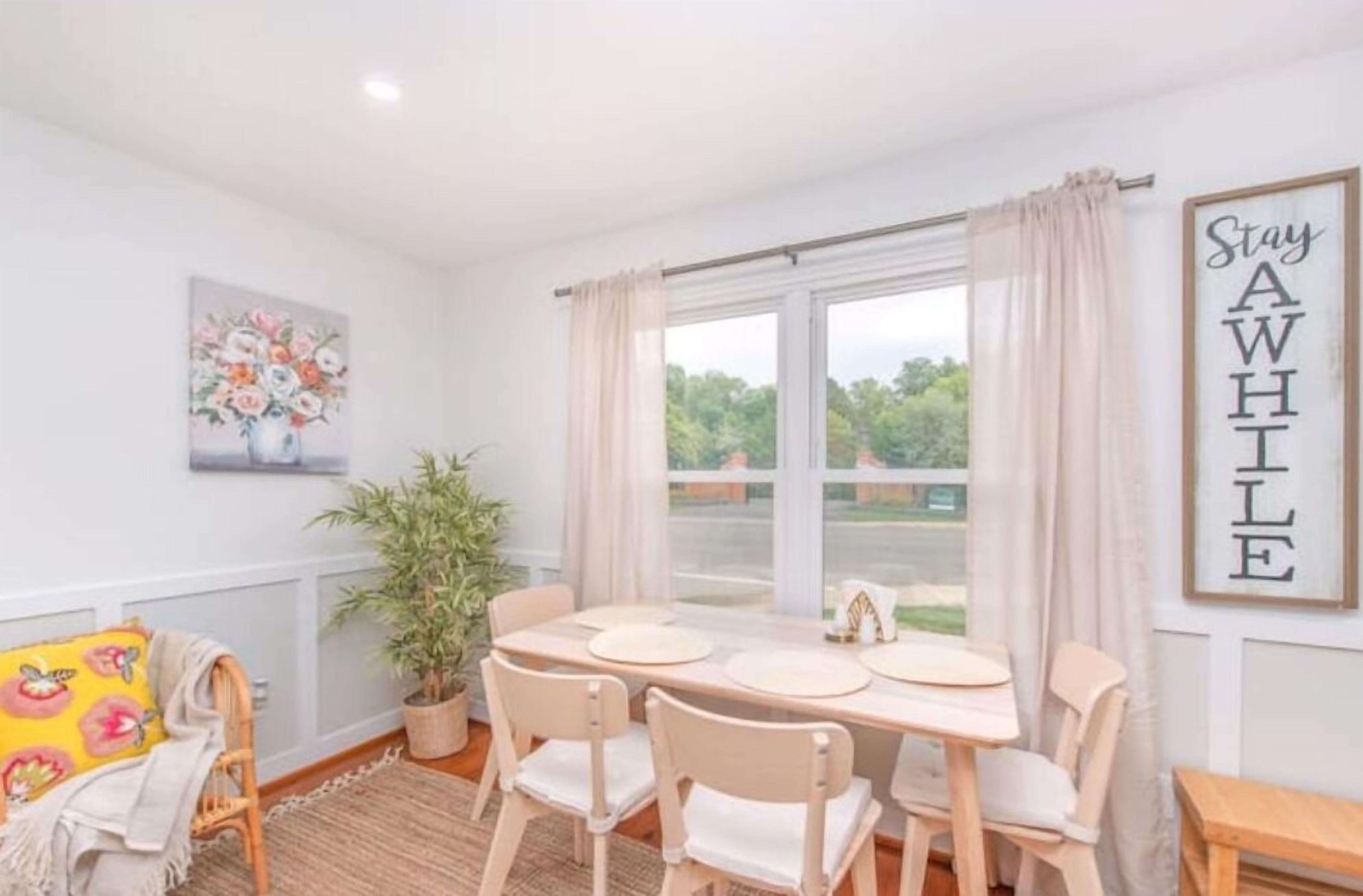 A dining area with a table set for four, a potted plant, and a view of greenery outside.
