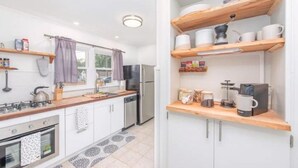 A modern kitchen with white cabinets, a stainless steel refrigerator, and wooden shelves above the counter.