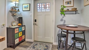 A small dining area with a round wooden table and two stools, a colorful bird-themed dresser, a lamp, and a door with a window. - 3 Mi to Dtwn: Convenient Denver Apt (Denver)
