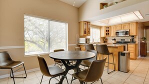 Una cucina moderna con mobili in legno, un forno a microonde in acciaio inossidabile e un tavolo da pranzo rotondo con sei sedie.