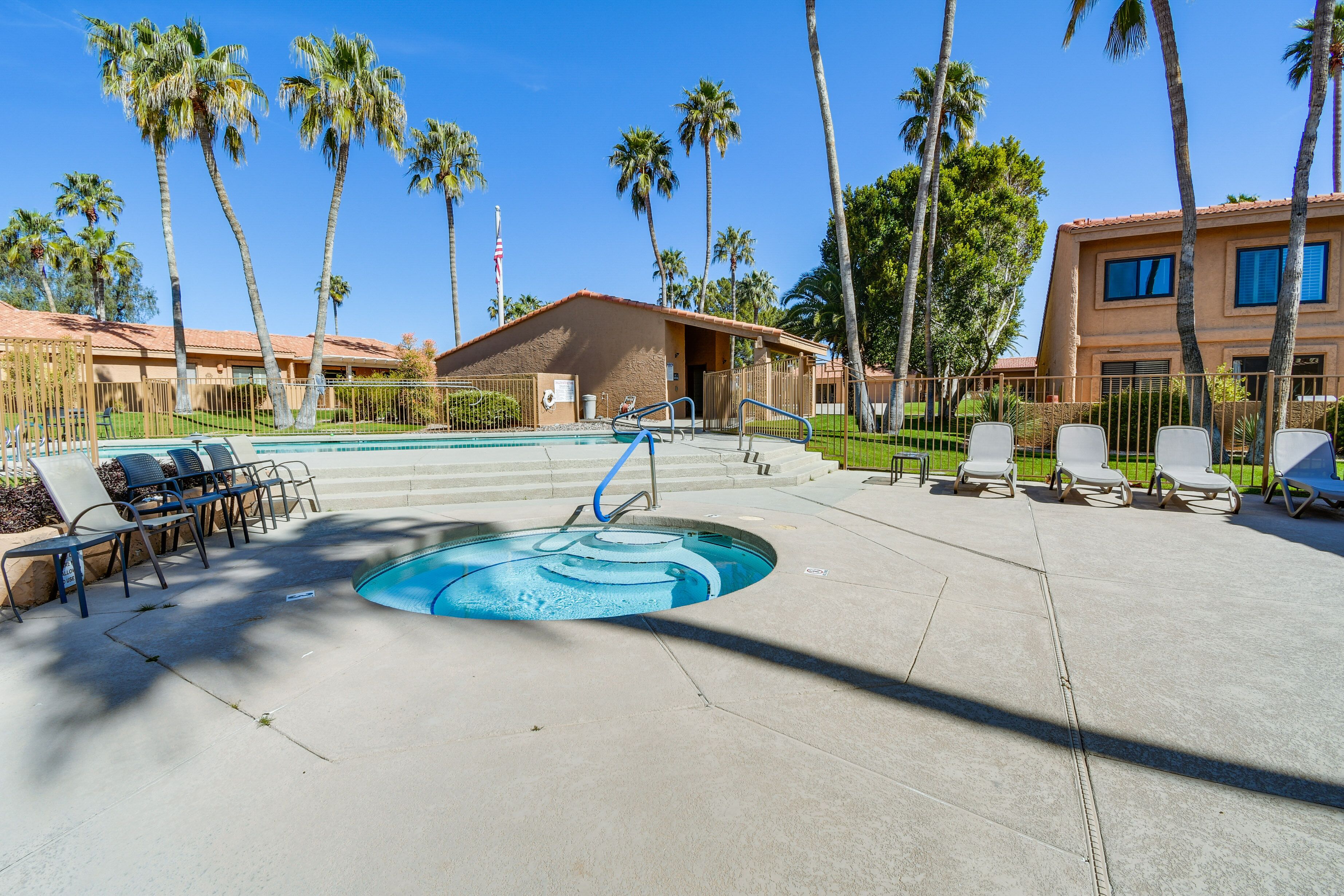 A pool area with lounge chairs, palm trees, and a building with a red-tiled roof.