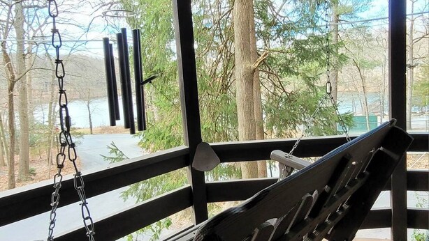 A wooden swing suspended by chains in a covered outdoor area with a view of trees and a body of water. - Quiet Historic Cottage ▪︎ Spacious 4br Mount Gretna Retreat  (Mount Gretna)