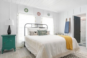 Un dormitorio con cama, mesita de noche, lámpara y puerta que da a otra habitación.