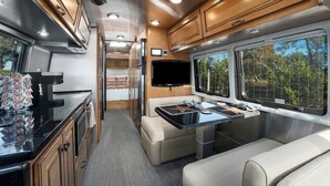 Interior compacto de una caravana con kitchenette, zona de estar y televisor.