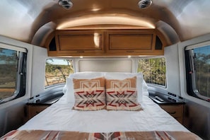 Un lit avec des coussins à motifs, une fenêtre donnant sur un beau paysage et une étagère au-dessus du lit.