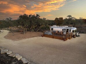 Un camping-car à l’arrêt, situé dans un espace abrité, entouré d’arbres et bordé d’un chemin de gravier.